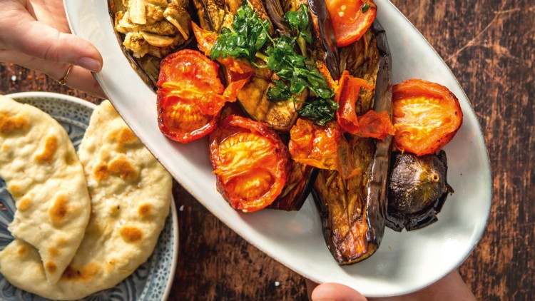 Ofen-Auberginen mit Kräutern, Tomaten und Pilzen auf weißer Platte, daneben Naan-Brot, Zucchini-Streifen und Schälchen mit Kirschtomaten.