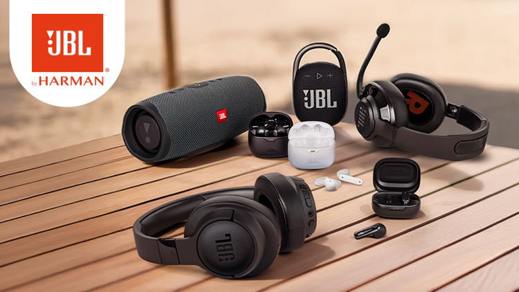 Mehrere JBL Audiogeräte wie Lautsprecher, Kopfhörer und Ohrhörer auf einem Holztisch, Logo JBL by HARMAN links oben.
