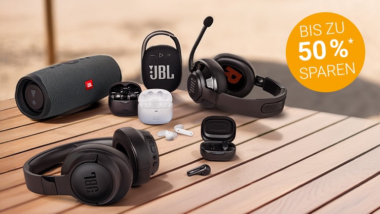 Mehrere schwarze und weiße Audiogeräte von JBL liegen auf einem Holztisch, daneben orange Kreis mit „Bis zu 50 %* sparen“.