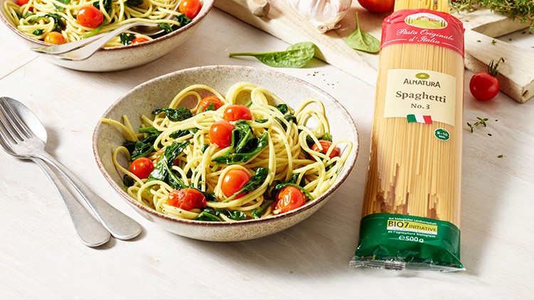 Zwei Schalen mit Spaghetti, Spinat und Kirschtomaten neben einer Packung Alnatura Spaghetti auf einem hellen Tisch.