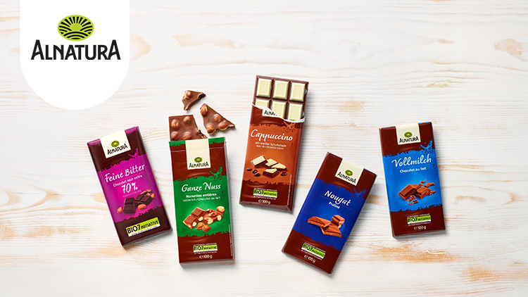 Fünf Alnatura-Schokoladensorten in Verpackungen mit den Sorten Feine Bitter, Ganze Nuss, Cappuccino, Nougat und Vollmilch.
