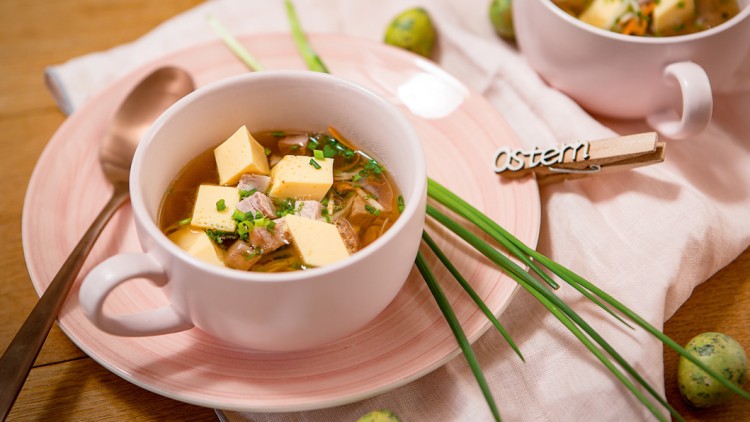 Eine Schale klare Suppe mit Tofu-Würfeln und Schnittlauch auf rosa Teller, dekoriert mit der Wäscheklammer „Ostern“.