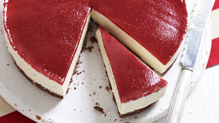Ein Kuchen mit weißer Creme und roter Glasur auf weißer Platte, ein Stück ist herausgeschnitten, daneben ein Messer.