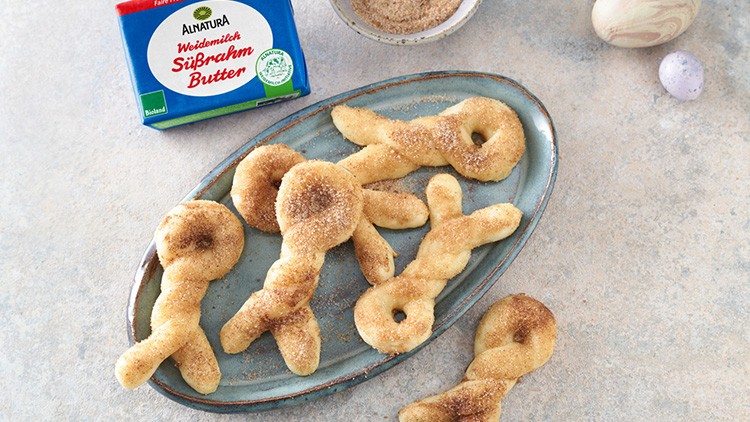Ein ovaler Teller mit Zimt-Zucker-Gebäck in Hasenform, daneben eine Butterpackung und eine Schale mit Zimt-Zucker.