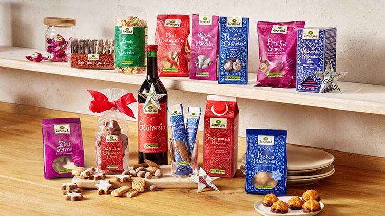 Auswahl an weihnachtlichen Lebensmitteln wie Glühwein, Keksen, Pralinen und Tee auf einem Tisch und einem Regal arrangiert.