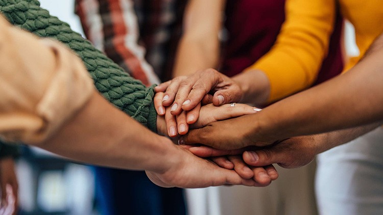 Mehrere Hände verschiedener Personen liegen übereinander als Zeichen von Gemeinschaft und Zusammenarbeit.
