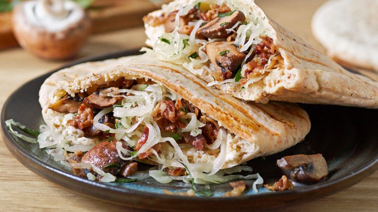 Vollkorn-Pita-Taschen gefüllt mit sautierten Champignons, Sauerkraut und Petersilie auf einem dunklen Teller.
