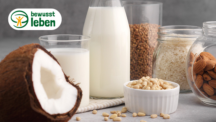Eine halbierte Kokosnuss, ein Glas Pflanzenmilch, Mandeln, Reis, Buchweizen und das Logo „bewusst leben“ mit grünem Schriftzug.