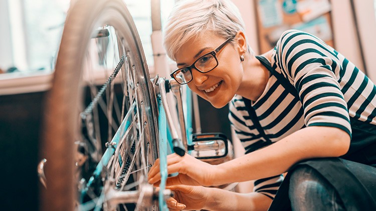 Person repariert ein Fahrrad und justiert die Kette mit beiden Händen in einer Werkstattumgebung.