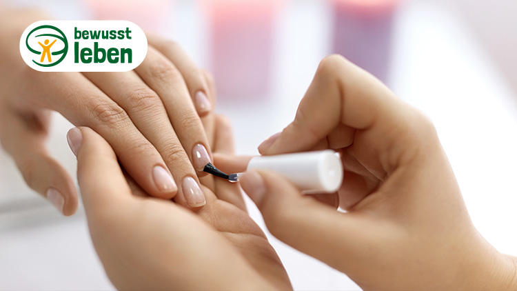 Eine Hand wird mit hellem Nagellack lackiert, oben links steht das Logo „bewusst leben“ mit grünem Text und orangener Figur.