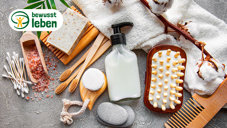 Wellness-Accessoires wie Bürste, Kamm, Wattestäbchen und Fläschchen auf grauem Untergrund, oben links Logo „bewusst leben“.