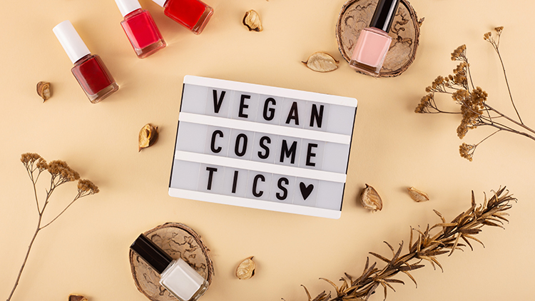 Leuchtkasten mit der schwarzen Aufschrift „VEGAN COSMETICS“ und Herz-Symbol, umgeben von Nagellack und Trockenblumen.