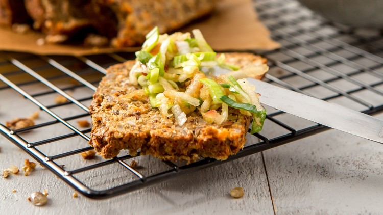 Eine Scheibe Körnerbrot mit geraspeltem Gemüse und Frühlingszwiebeln belegt liegt auf einem schwarzen Kuchengitter.