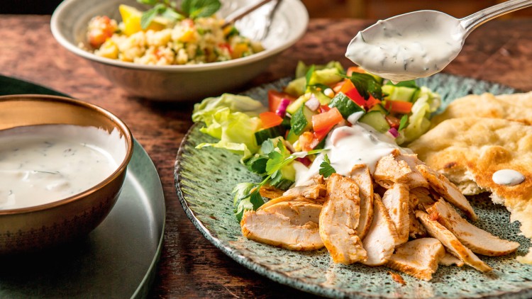 Grillhähnchen, Salat, Fladenbrot und Tzatziki auf einem Teller, daneben Schale mit Tzatziki und eine Schüssel mit Couscous-Salat.