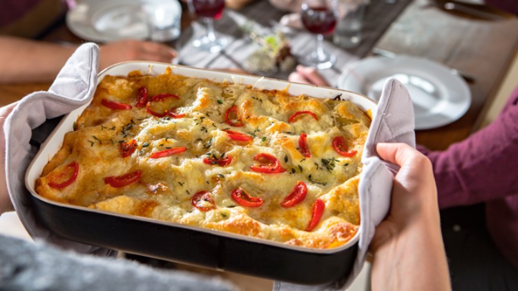 Eine rechteckige Auflaufform mit goldbraun überbackenem Auflauf aus Käse, Tomatenscheiben und Kräutern wird serviert.