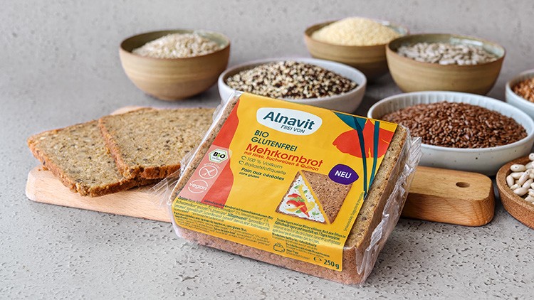 Verpacktes glutenfreies Bio-Mehrkornbrot von Alnavit, daneben zwei Brotscheiben und kleine Schalen mit Körnern.