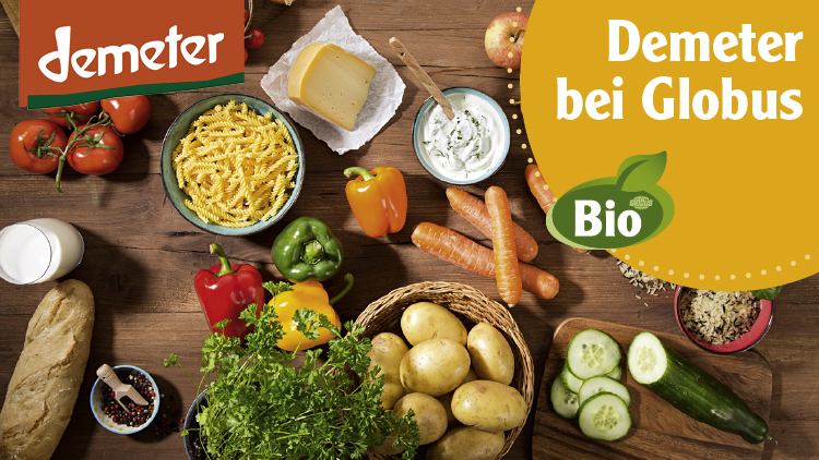 Auf einem Holztisch liegen Demeter-Lebensmittel wie Gemüse, Nudeln, Käse, Reis, Brot, Milch, Äpfel, Eier und Kräuter, Text: Demeter bei Globus, Bio.