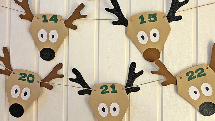 Fünf Rentier-Gesichter aus Papier mit schwarzen Nasen, Augen und den Zahlen 14, 15, 20, 21, 22 hängen an einer Wand.