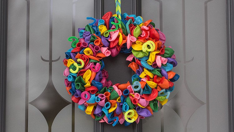 Bunter Kranz aus vielen unterschiedlich farbigen Luftballons hängt vor einer Tür mit Glas und dekorativen Metallstreben.