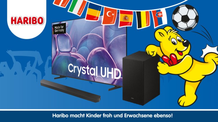 Gelber Bär mit Zuckertüte kickt einen Fußball, daneben ein Fernseher mit der Aufschrift „Crystal UHD“, eine Soundbar und ein Lautsprecher.