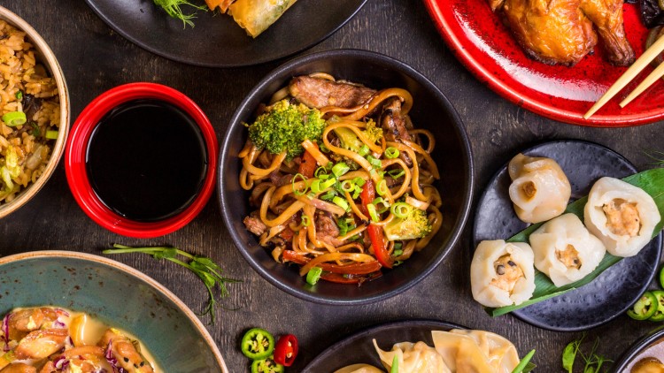 Verschiedene asiatische Gerichte wie gebratene Nudeln, Frühlingsrollen, Dumplings und Reis auf bunten Tellern mit Sojasoße.