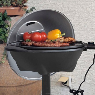 Ein runder Elektrogrill mit geöffnetem Deckel, darauf grillen Würstchen, Fleisch, rote Tomaten und eine gelbe Paprika.