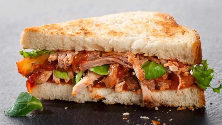 Getoastetes Sandwich mit Salat, zartem Fleisch sowie roter Sauce, serviert auf einer dunklen Steinplatte.