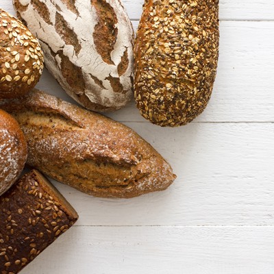 Mehrere Brotsorten, darunter Körnerbrot und Krustenbrot, liegen auf einem hellen, weißen Holzuntergrund.
