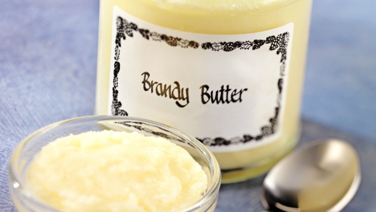 Ein Glas mit der Aufschrift Brandy Butter steht neben einer kleinen Glasschale mit Buttercreme und einem Löffel.