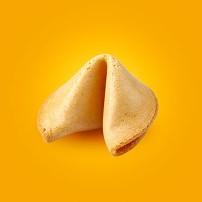 Ein hellbrauner Glückskeks liegt vor einem einfarbig gelben Hintergrund.