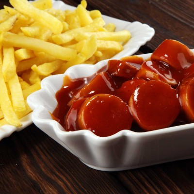Gebratene Pommes frites und Currywurst in Tomatensoße, serviert in weißen Schalen auf dunklem Holzuntergrund.