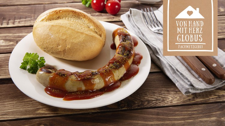 Gegrillte Bratwurst mit Currysauce und Petersilie auf einem weißen Teller, daneben ein Brötchen, Messer, Gabel und Logo „Von Hand mit Herz GLOBUS Fachmetzgerei“.