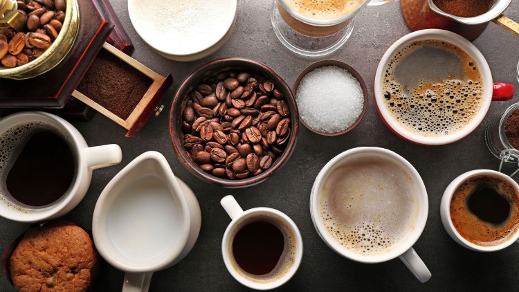 Verschiedene Tassen mit unterschiedlichem Kaffee, Kaffeebohnen, Kaffeepulver, Zucker, Milch und ein Keks auf dunklem Untergrund.