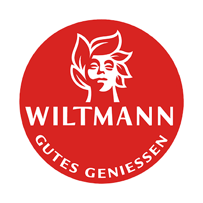Roter Kreis mit weißem Gesicht einer Frau und den Schriftzügen „WILTMANN“ und „GUTES GENIESSEN“.