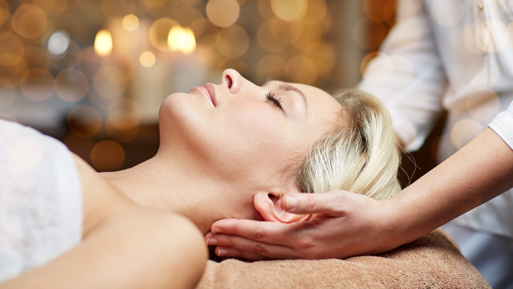 Person erhält eine Nackenmassage, Kerzenlicht und goldene Lichter im Hintergrund schaffen eine entspannte Atmosphäre.