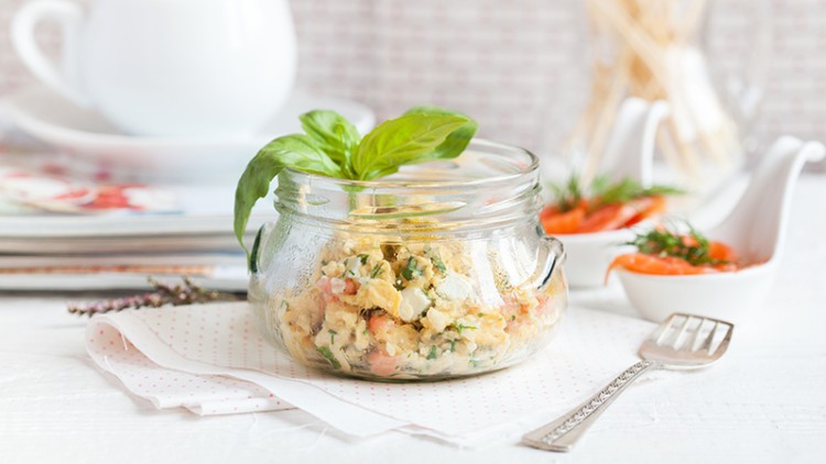 Frischer Salat mit Gemüse und Kräutern in einem Glas, dekoriert mit Basilikumblättern, auf einem weißen Tisch mit Gedeck.
