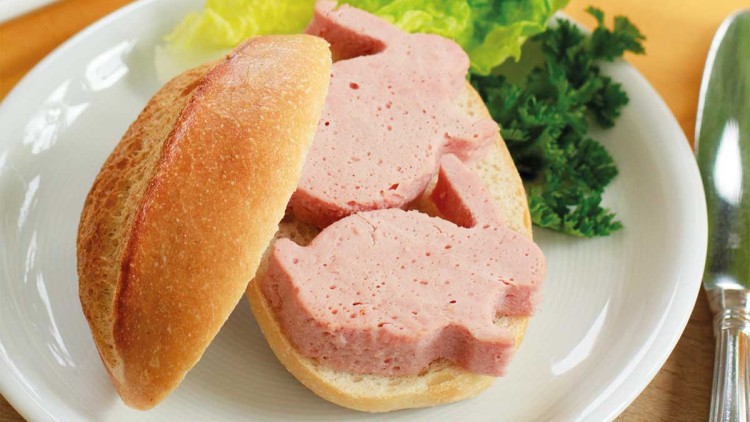 Brötchenhälfte mit Wurstscheiben in Hasenform, Salatblatt und Petersilie auf einem Teller, daneben ein Ei im Eierbecher.