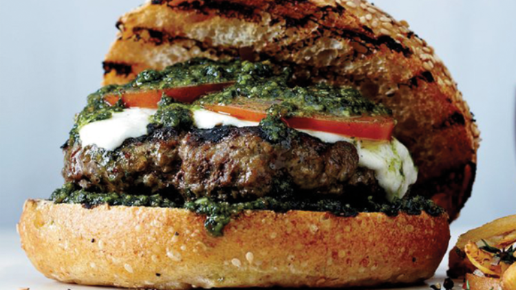 Gegrillter Burger mit Fleischpatty, Mozzarella, Tomatenscheiben und grüner Sauce in Sesambrötchen, daneben Pommes.