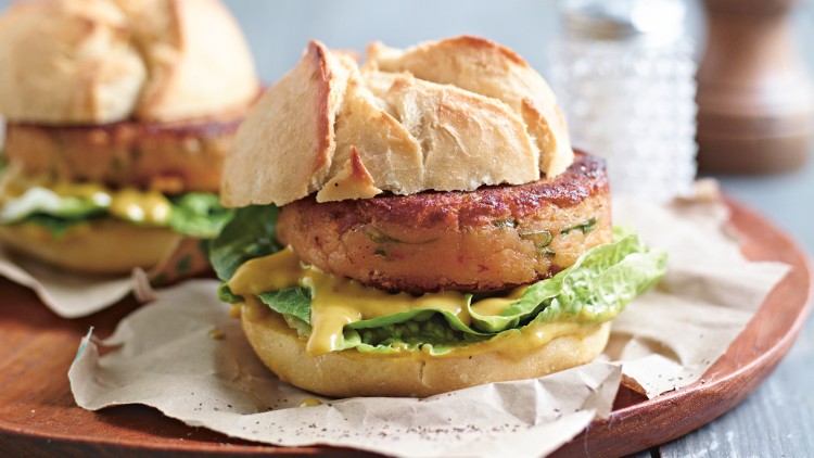 Zwei Burger mit Brötchen, Gemüse-Patty, Salat und Sauce liegen auf Backpapier auf einem hölzernen Teller.