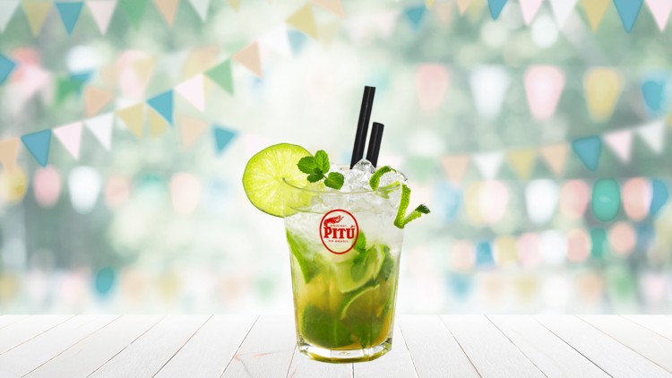 Ein Glas mit Limetten, Minze, Eiswürfeln, zwei schwarzen Strohhalmen und Logo „PITÚ“ steht vor einer bunten Wimpelgirlande.