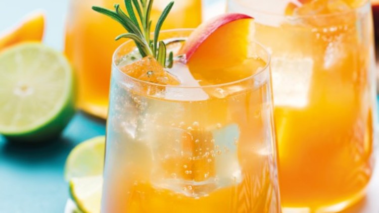 Gläser mit orangefarbenem Getränk, Rosmarinzweig, Eiswürfeln und Pfirsichstücken, daneben Limettenhälften auf blauem Hintergrund.