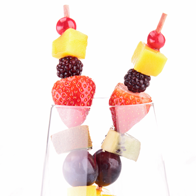 Zwei Fruchtspieße mit Erdbeeren, Mango, Brombeeren, roter Weintraube und Kirsche stecken in einem durchsichtigen Glas.