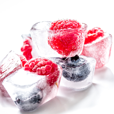 Gefrorene Himbeeren und Blaubeeren sind in durchsichtigen Eiswürfeln auf weißem Hintergrund eingeschlossen.