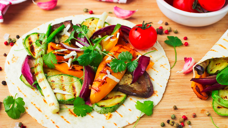 Weizentortilla mit gegrilltem Gemüse wie Paprika, Zucchini und Aubergine, garniert mit frischen Kräutern und einer Kirschtomate.