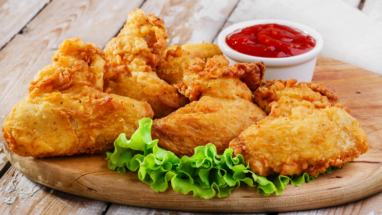 Knusprig frittierte Hähnchenteile mit frischem grünem Salat und einer weißen Schale Ketchup auf einem Holzbrett.