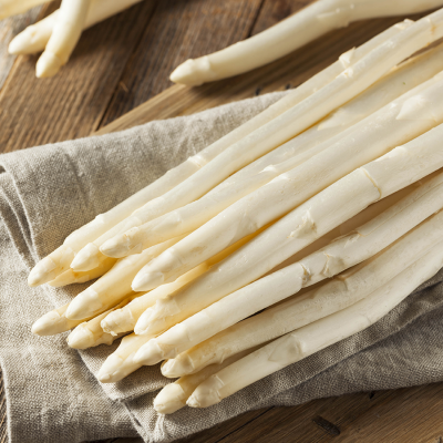 Mehrere Stangen weißer Spargel liegen auf einem beigen Stofftuch, das auf einer Holzoberfläche ausgebreitet ist.