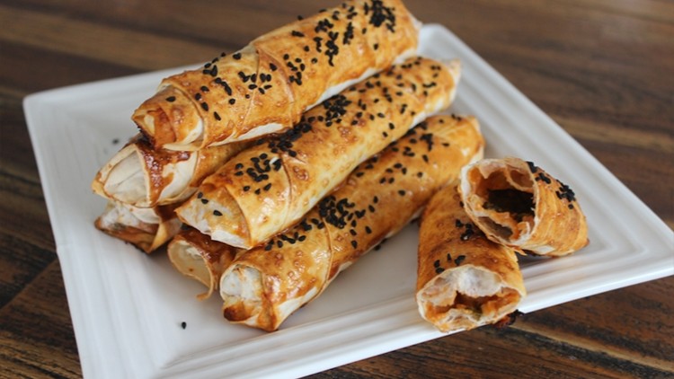 Mehrere goldbraune Teigröllchen mit schwarzem Sesam gefüllt mit weißer Creme auf quadratischem, weißen Teller.