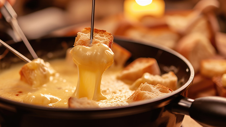 Geschmolzener Käse in einem Fonduetopf, in den ein Stück Baguette an einer Fonduegabel eingetaucht wird.