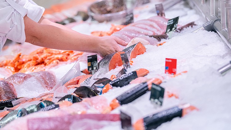 Eine Hand greift nach einem Stück Lachs in einer Kühltheke mit Eis, auf der verschiedene Fischsorten liegen.