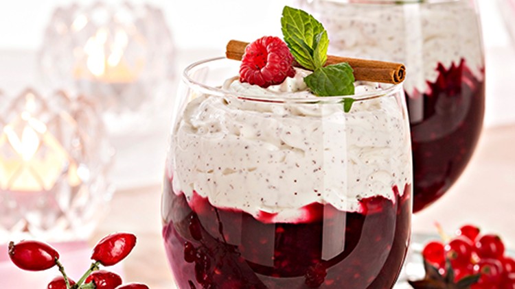 Zwei Gläser mit Schichtdessert aus roter Fruchtsoße und Sahnecreme, garniert mit Himbeere, Minze und Zimtstange.